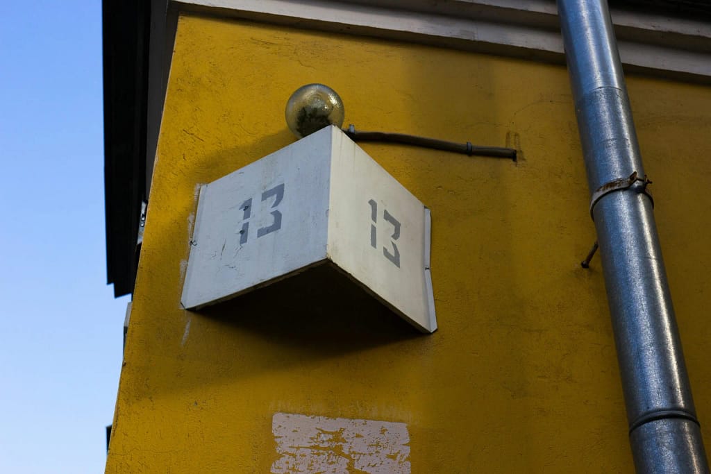 Low angle view of number 13 sign on a retro yellow building wall under clear blue sky.