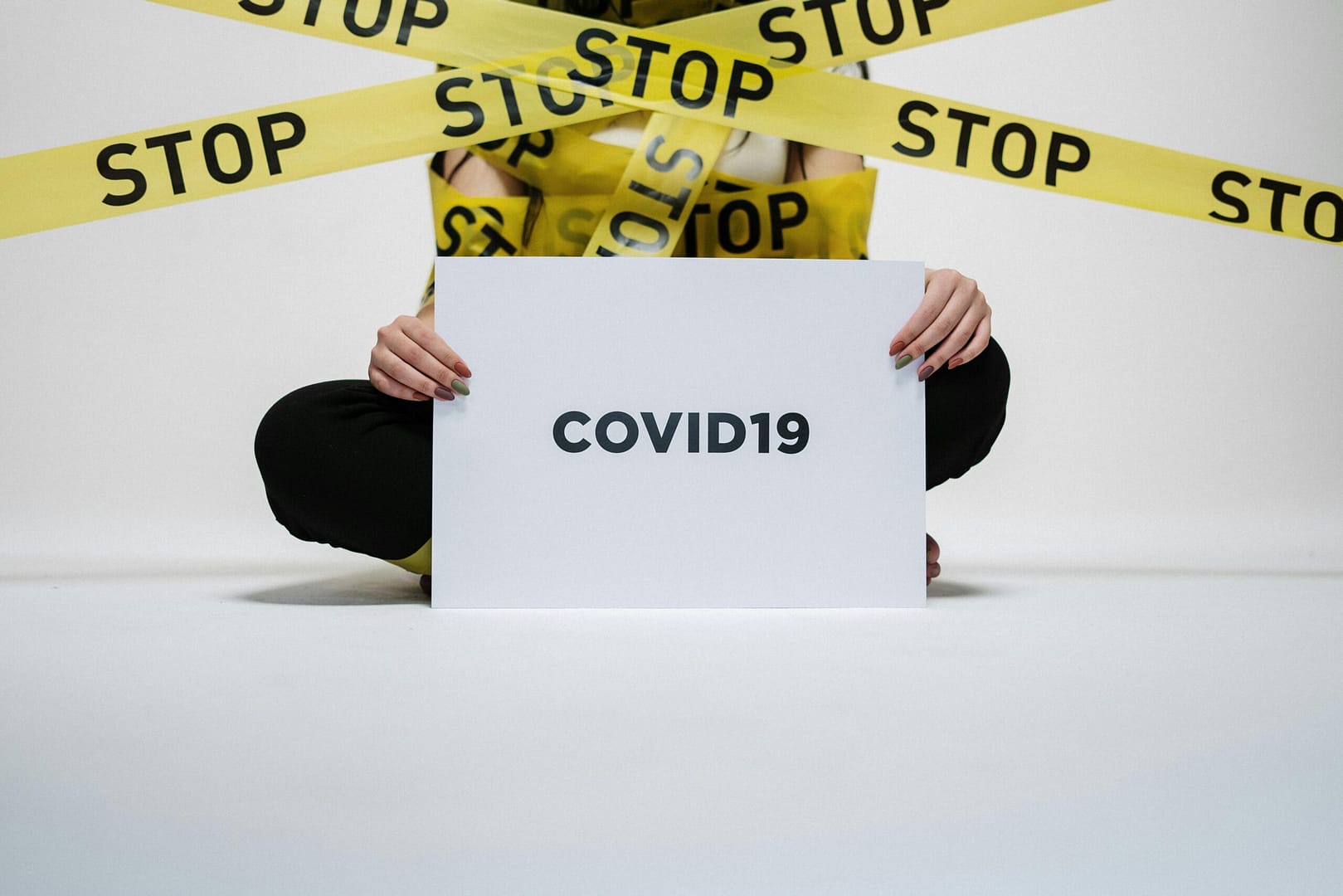 Person holding COVID-19 sign surrounded by yellow stop tape, symbolizing quarantine and safety.